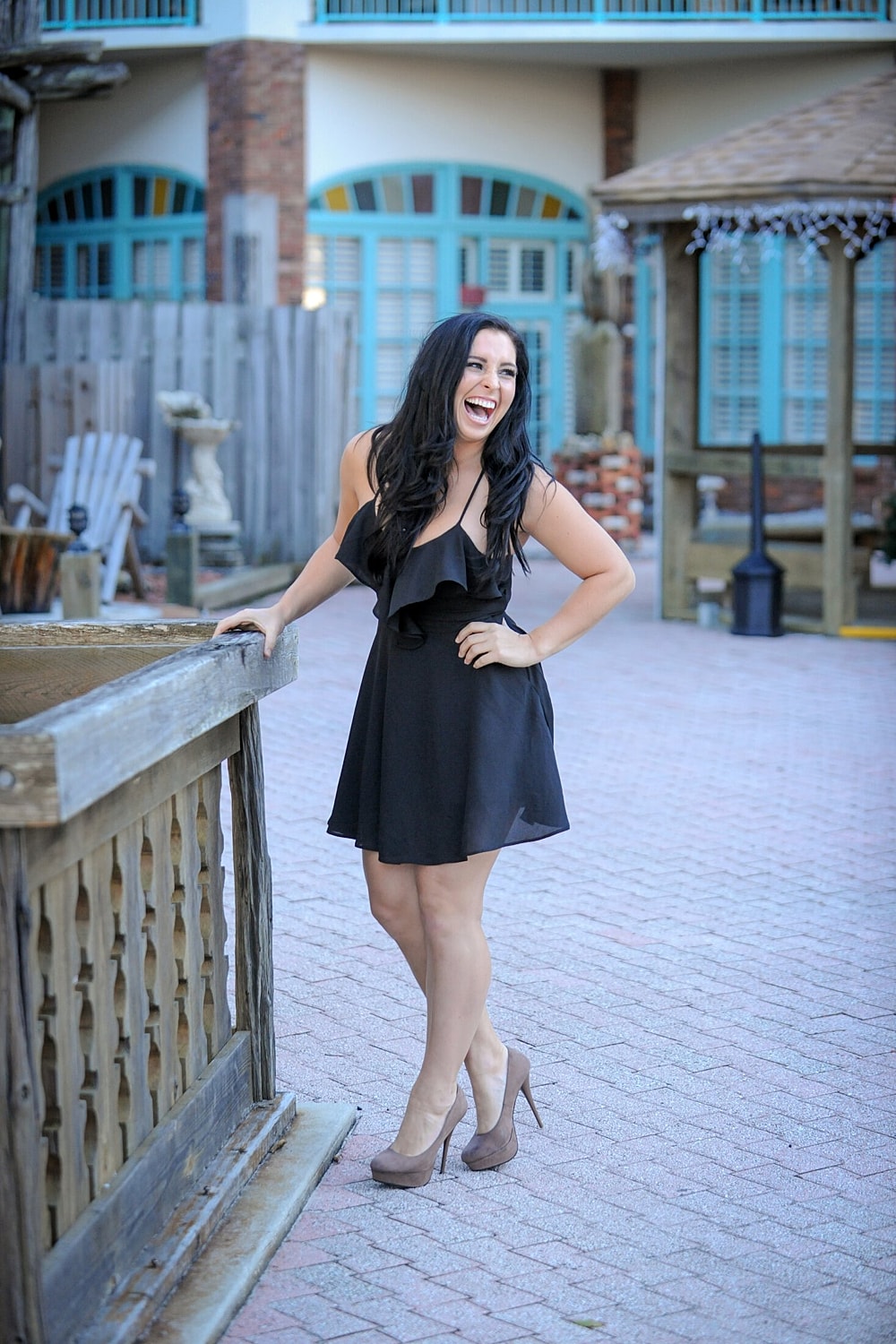 Woman in a black dress laughing outdoors.