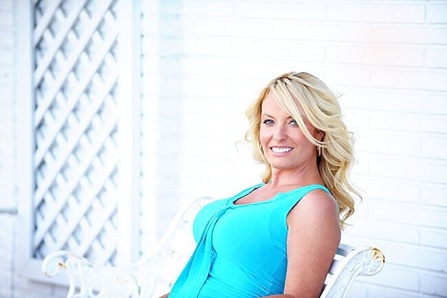 Smiling woman in blue dress sitting outside.