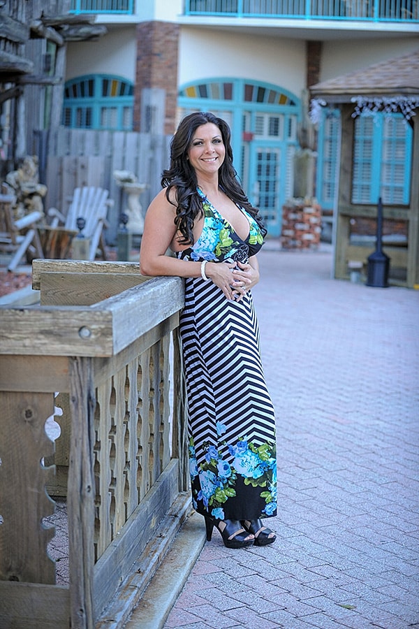 Woman in floral dress posing by wooden railing.