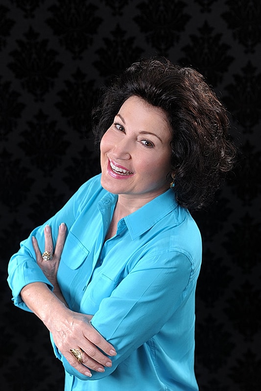 Smiling woman in blue shirt against dark background.