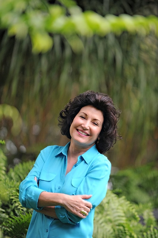 Smiling woman in blue shirt among greenery.