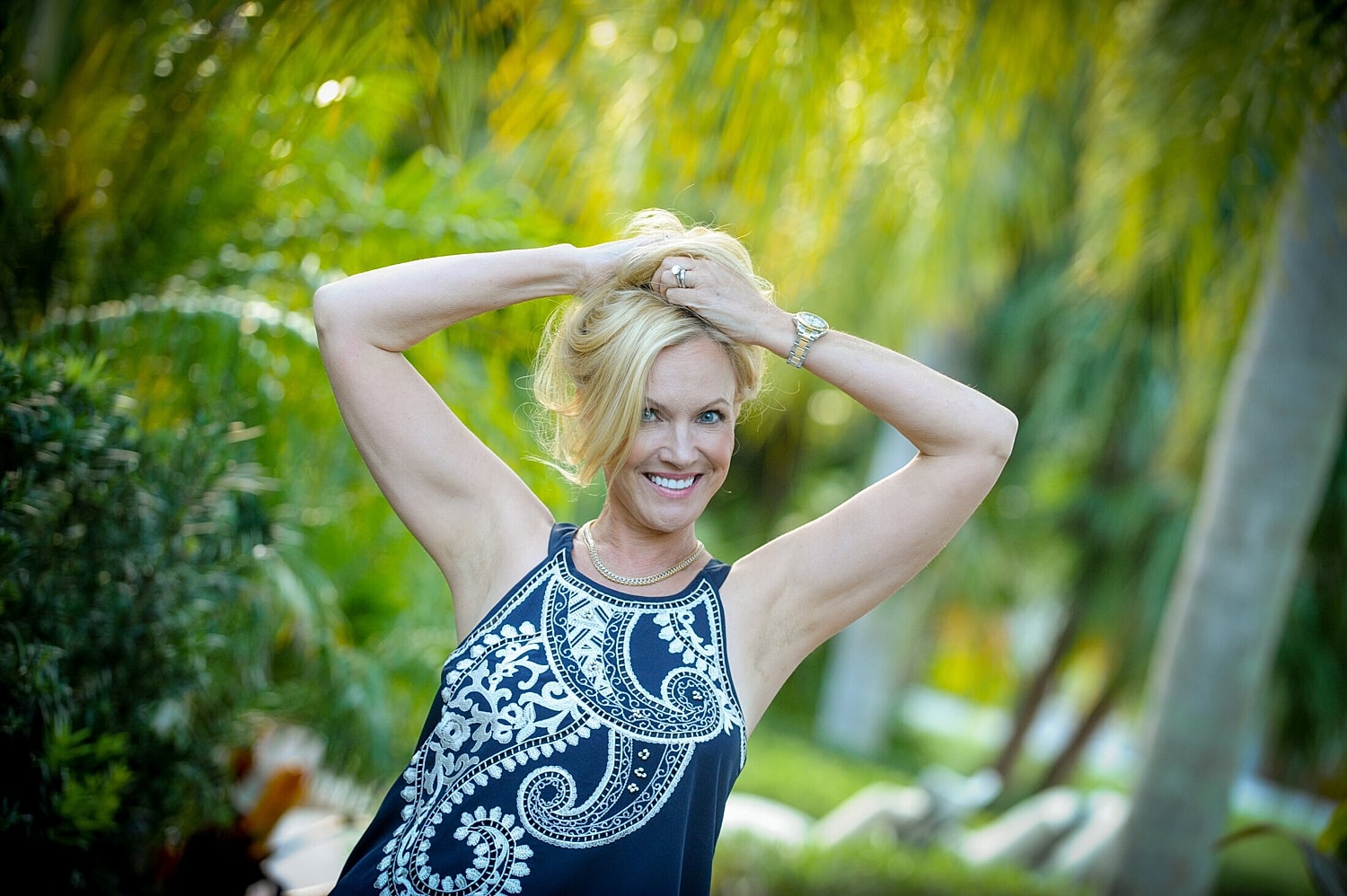 Smiling woman posing outdoors with greenery background.