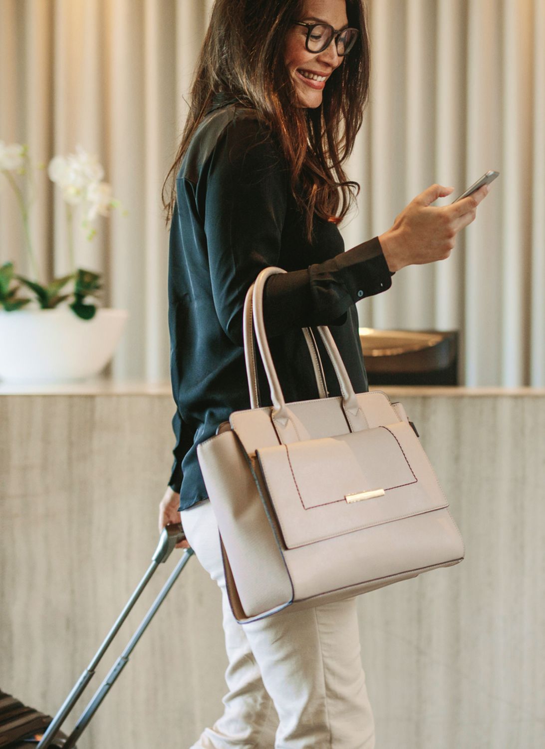 Woman with bag checking phone in modern setting.
