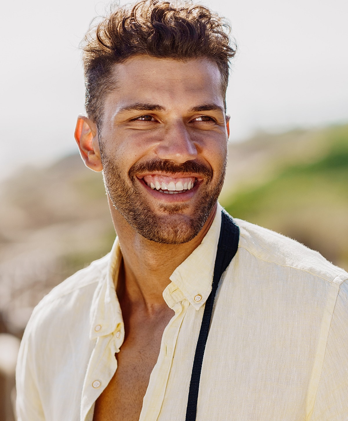 Smiling man in yellow shirt outdoors.