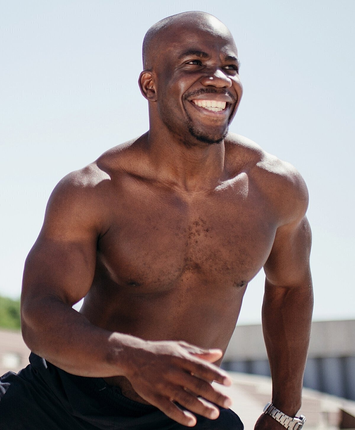 Smiling man running outdoors, shirtless, energetic.